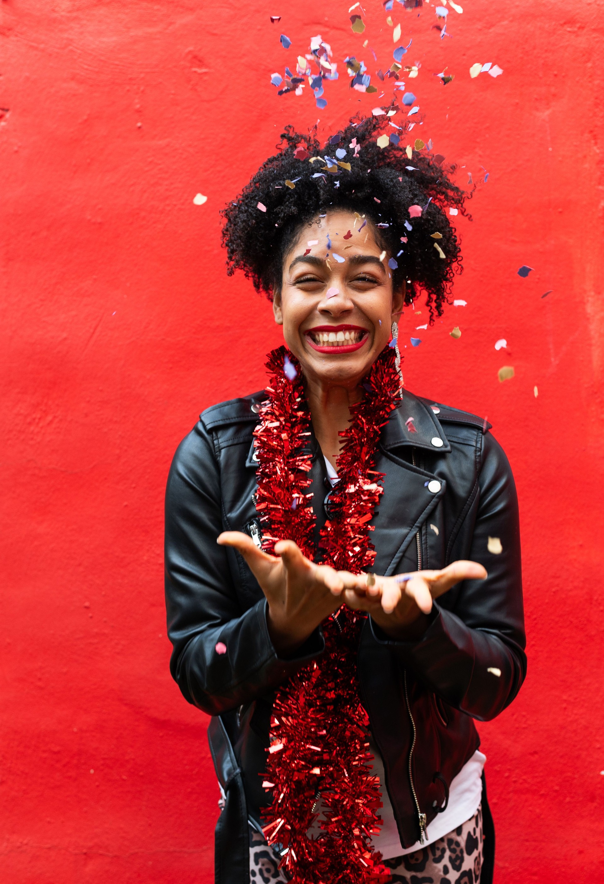 Young woman catching confetti at party with red background
